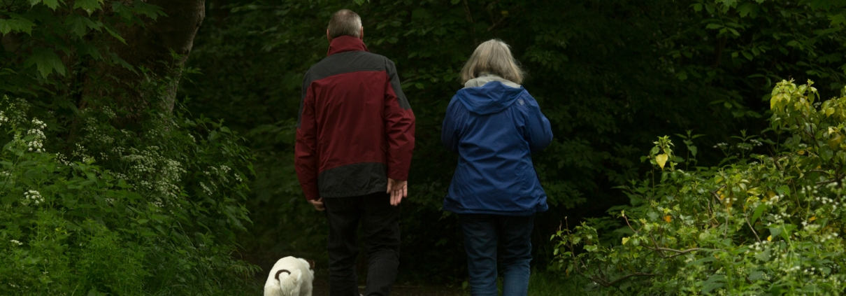 a couple walking through the woods with a dog