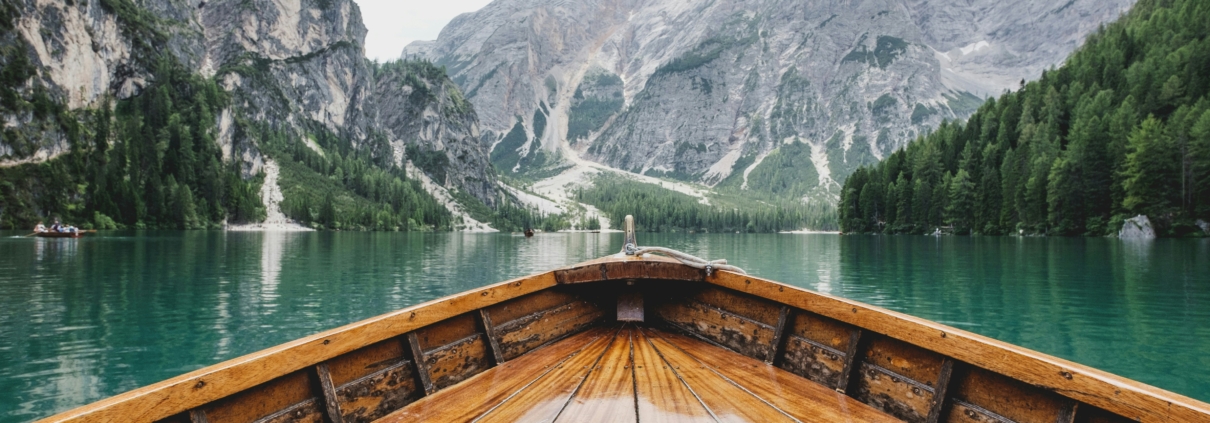 a picture of a wooden boat traveling through a river surrounded by snow covered mountains