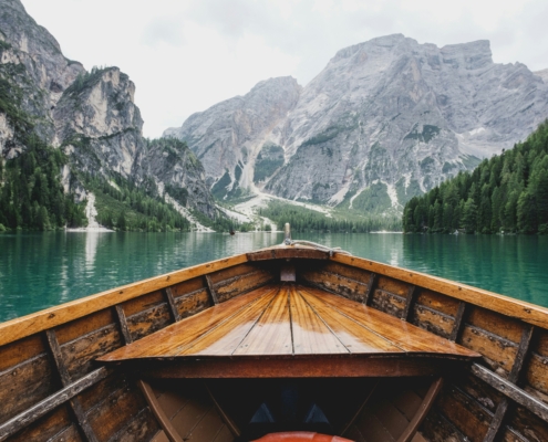 a picture of a wooden boat traveling through a river surrounded by snow covered mountains